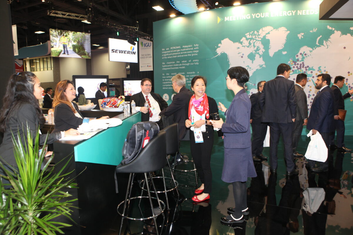group of people stood in suits talking to each other at a trade show. The main characters are two women who are smiling at each other in active conversation. This is an example of how neuroscience should be used to understand attendee dynamics and retention. 